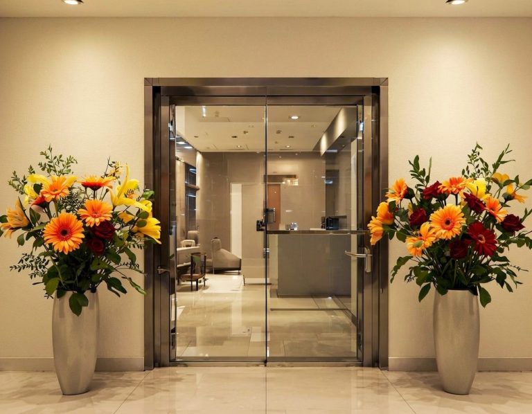 Eingang mit Glastüren, verziert mit bunten Blumenarrangements auf beiden Seiten.