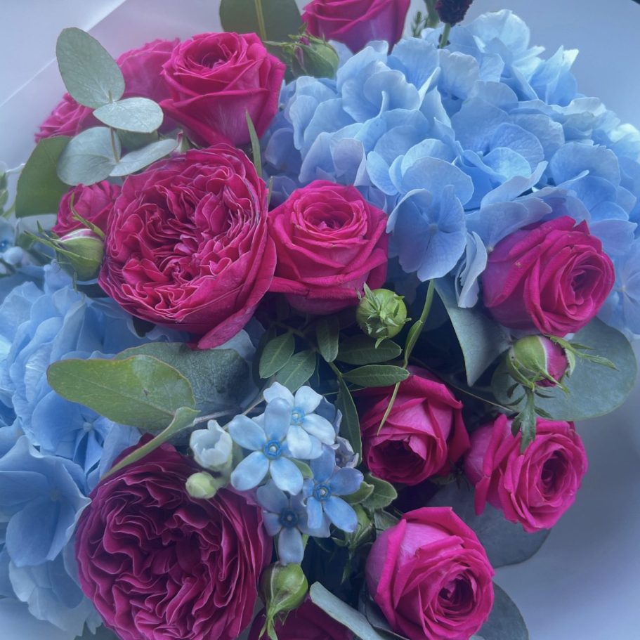 Bunter Blumenstrauß in einer Glasvase mit rosa und lila Blüten, umgeben von grünen Blättern.